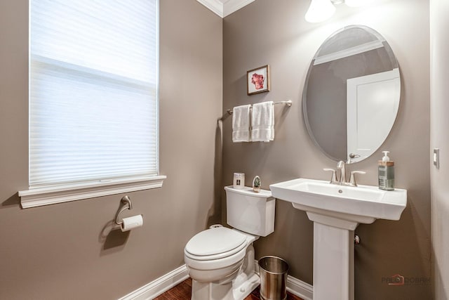 half bath with ornamental molding, baseboards, toilet, and wood finished floors