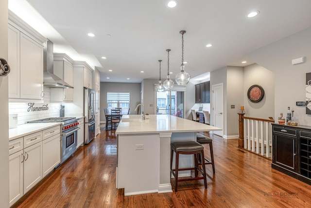 kitchen featuring a sink, a center island with sink, recessed lighting, high end appliances, and wall chimney range hood