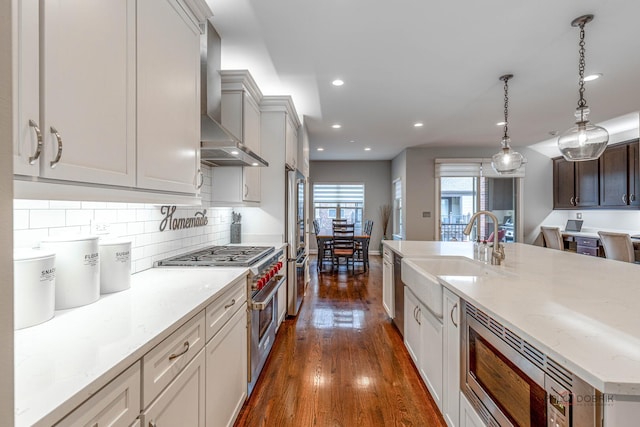 kitchen featuring wall chimney range hood, high quality appliances, a sink, dark wood-style flooring, and recessed lighting
