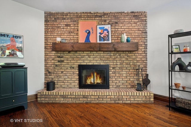 unfurnished living room featuring a brick fireplace, baseboards, and wood finished floors