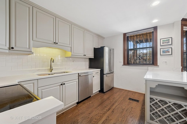 kitchen featuring visible vents, dark wood-type flooring, a sink, backsplash, and stainless steel appliances