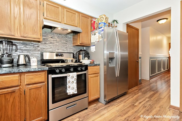 kitchen with appliances with stainless steel finishes, under cabinet range hood, dark countertops, tasteful backsplash, and light wood-type flooring