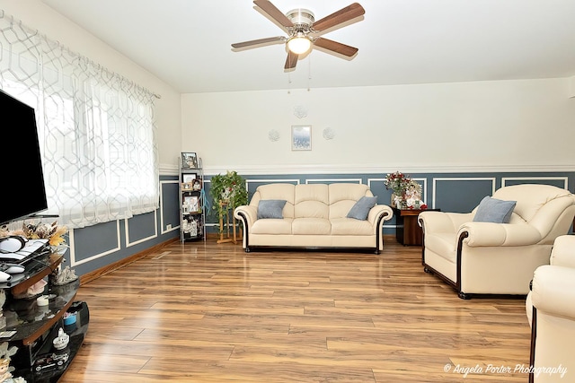 living room with a decorative wall, wainscoting, ceiling fan, and wood finished floors