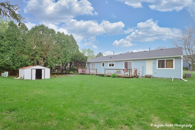 rear view of house with a lawn, an outbuilding, a wooden deck, and a storage unit