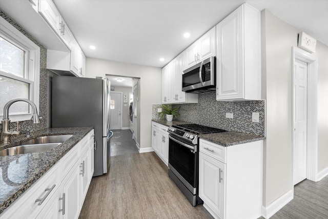 kitchen with white cabinets, stainless steel appliances, a sink, baseboards, and tasteful backsplash