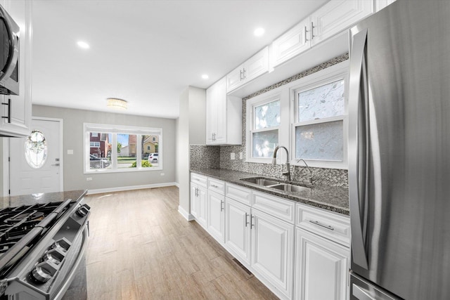 kitchen featuring dark stone countertops, a sink, light wood-type flooring, stainless steel appliances, and baseboards
