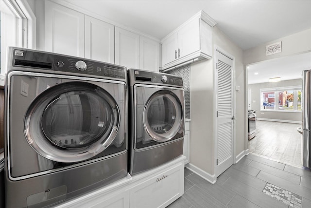 clothes washing area with baseboards, cabinet space, wood finished floors, and washer and clothes dryer