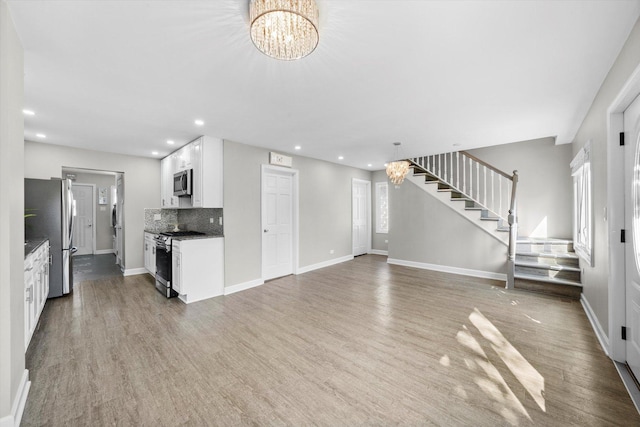 unfurnished living room with recessed lighting, wood finished floors, an inviting chandelier, and stairs