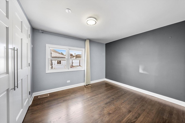 spare room with dark wood-type flooring, visible vents, and baseboards