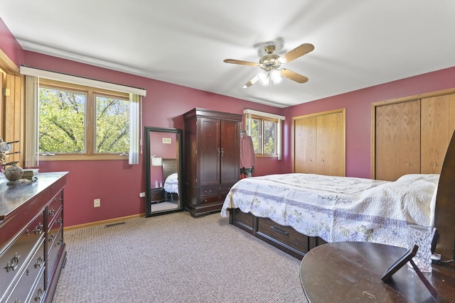 bedroom featuring baseboards, multiple closets, light colored carpet, and ceiling fan
