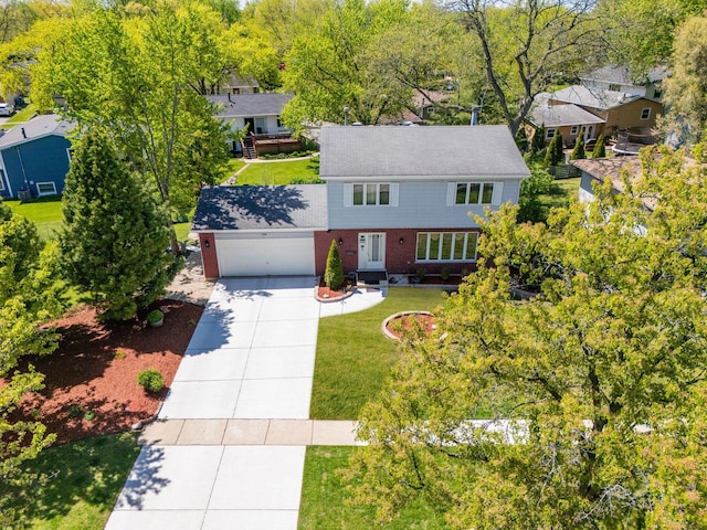 view of front of property with concrete driveway, brick siding, an attached garage, a front yard, and view of wooded area