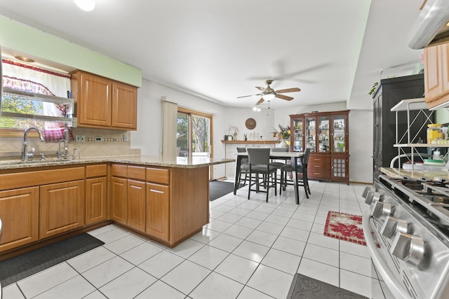kitchen with a sink, backsplash, a peninsula, ceiling fan, and light stone counters