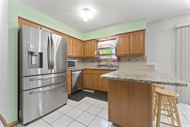 kitchen with stainless steel appliances, a peninsula, a sink, decorative backsplash, and light tile patterned flooring