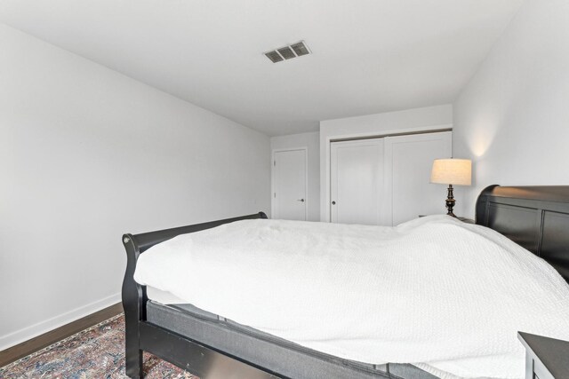 bedroom with baseboards, a closet, wood finished floors, and visible vents