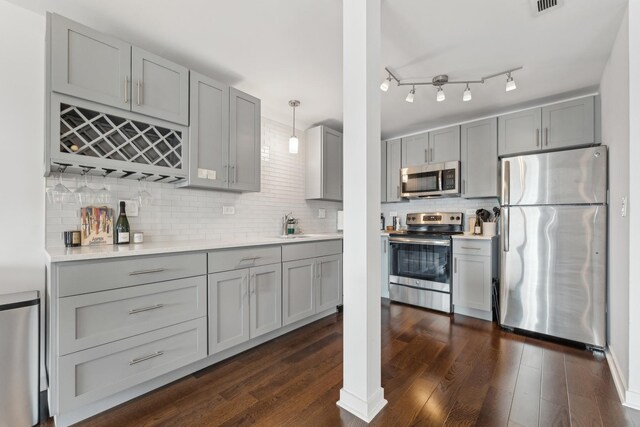 kitchen with gray cabinetry, appliances with stainless steel finishes, backsplash, and dark wood-style floors