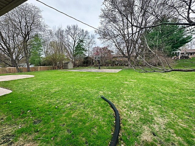 view of yard with fence, an outbuilding, basketball court, and a storage shed