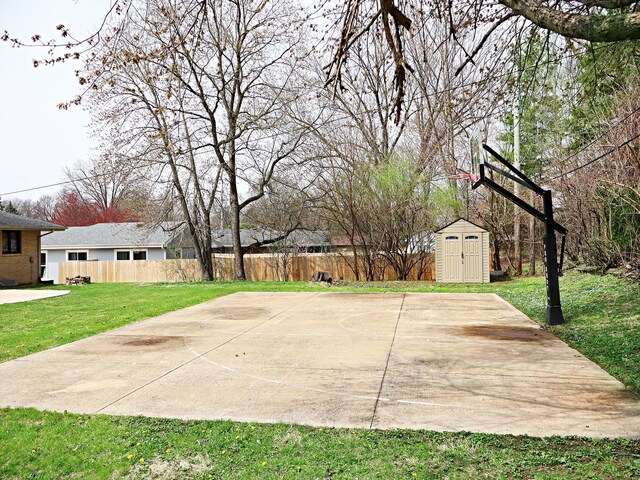 view of basketball court featuring a lawn, fence, a shed, and basketball hoop