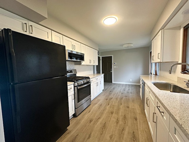 kitchen featuring a sink, light wood-type flooring, baseboards, appliances with stainless steel finishes, and white cabinetry