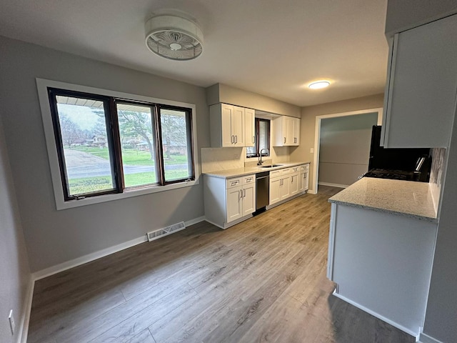 kitchen with a sink, light wood finished floors, visible vents, white cabinets, and dishwashing machine
