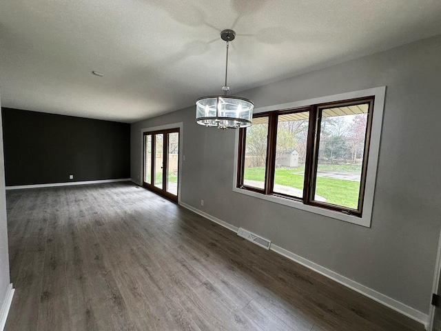 unfurnished dining area with baseboards, visible vents, a notable chandelier, and dark wood finished floors