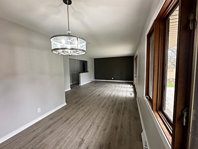 unfurnished dining area featuring dark wood-type flooring, baseboards, and a chandelier