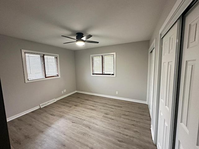 unfurnished bedroom featuring ceiling fan, baseboards, wood finished floors, and visible vents