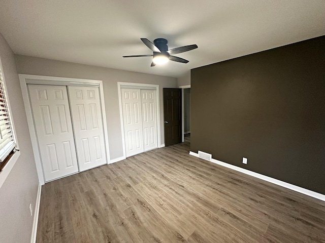 unfurnished bedroom featuring visible vents, baseboards, multiple closets, and wood finished floors