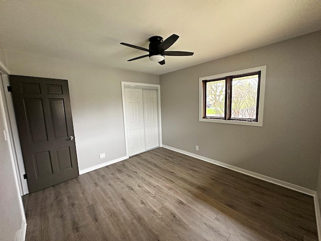 unfurnished bedroom with ceiling fan, baseboards, dark wood-style flooring, and a closet