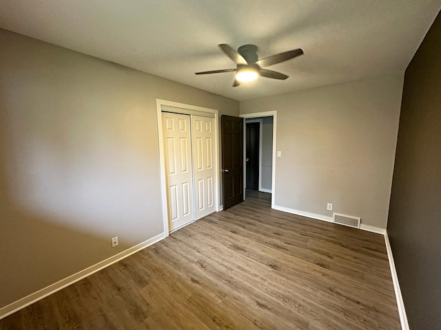 unfurnished bedroom with wood finished floors, visible vents, a closet, baseboards, and ceiling fan