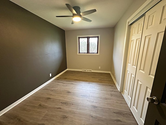 unfurnished bedroom featuring dark wood finished floors, baseboards, visible vents, a ceiling fan, and a closet