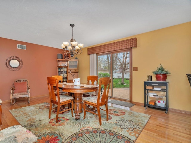 dining area featuring light wood-type flooring, baseboards, visible vents, and a notable chandelier