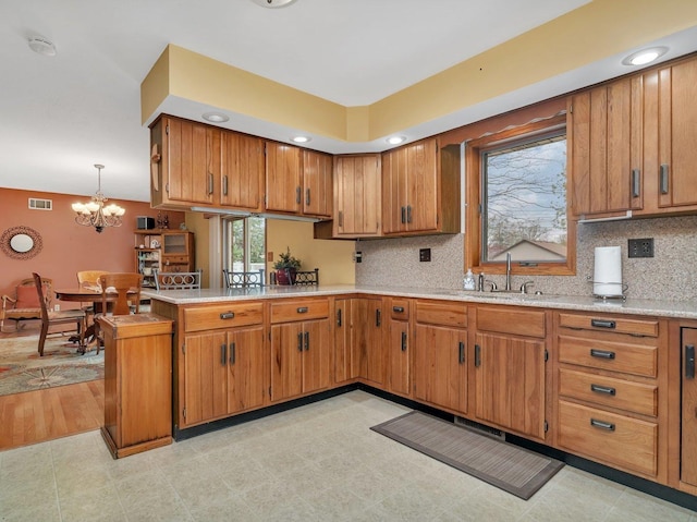 kitchen with brown cabinetry, light countertops, backsplash, and a peninsula