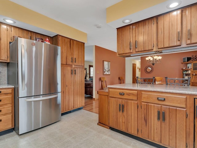 kitchen featuring light floors, light countertops, an inviting chandelier, freestanding refrigerator, and brown cabinetry