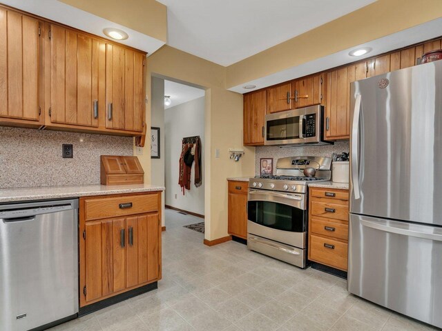 kitchen with brown cabinetry, decorative backsplash, stainless steel appliances, light countertops, and baseboards