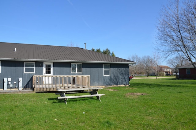 rear view of house featuring a wooden deck, a lawn, and metal roof