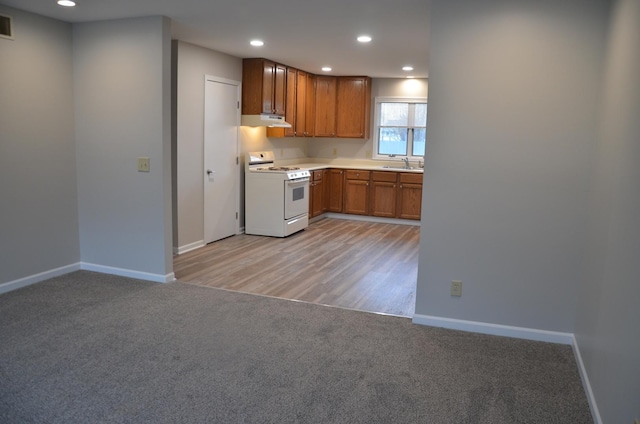 kitchen with baseboards, a sink, under cabinet range hood, white range with gas stovetop, and light carpet