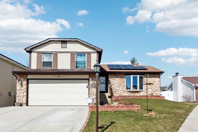 view of front of property with concrete driveway, solar panels, stone siding, a front yard, and a garage