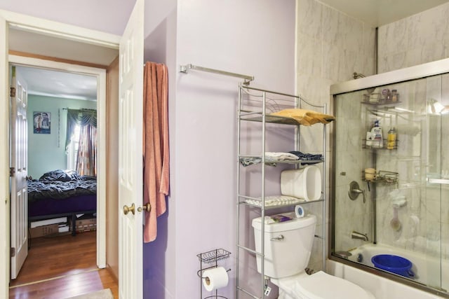 full bathroom with enclosed tub / shower combo, toilet, wood finished floors, and ensuite bathroom