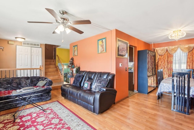 living area with stairs, ceiling fan with notable chandelier, visible vents, and light wood-style flooring