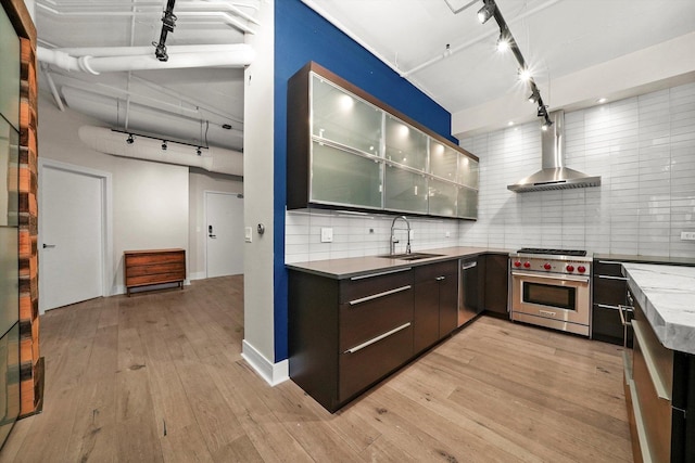 kitchen with a sink, designer stove, decorative backsplash, wall chimney range hood, and track lighting