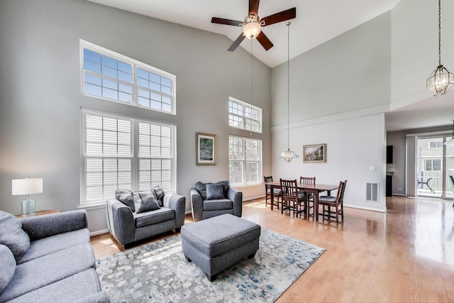 living room featuring visible vents, baseboards, high vaulted ceiling, light wood-type flooring, and a ceiling fan