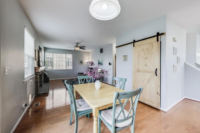 dining area with ceiling fan, a barn door, baseboards, light wood-type flooring, and visible vents