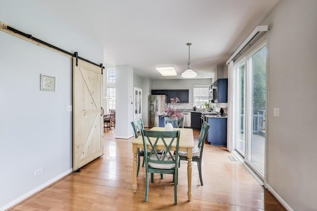 dining area featuring light wood-style floors, baseboards, and a barn door