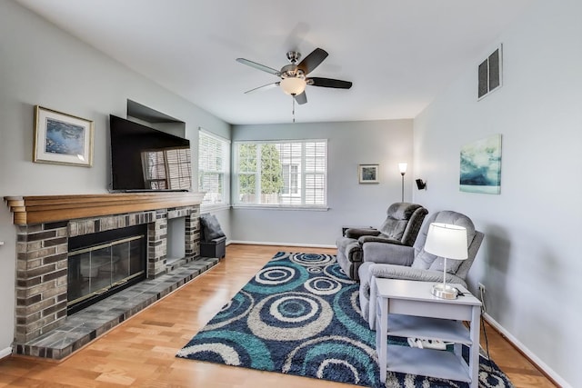living room featuring ceiling fan, a brick fireplace, baseboards, wood finished floors, and visible vents