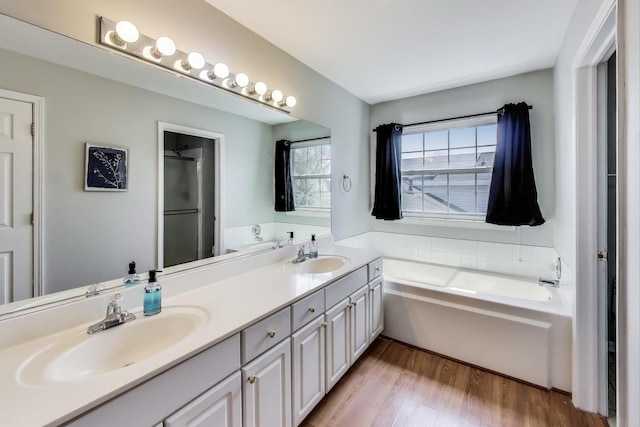 full bath featuring a garden tub, a sink, wood finished floors, and double vanity