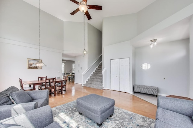 living room featuring a high ceiling, stairs, ceiling fan, and wood finished floors