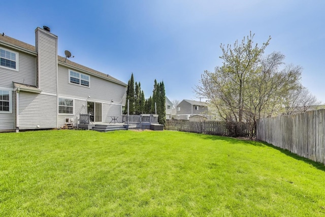 back of property with a yard, a wooden deck, a fenced backyard, and a chimney