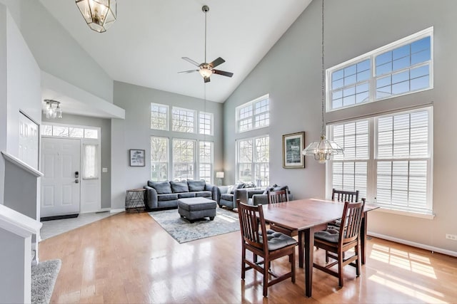 dining room with high vaulted ceiling, wood finished floors, and ceiling fan with notable chandelier