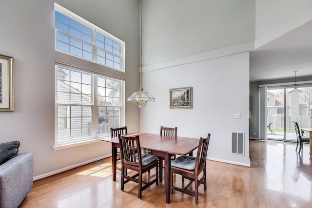 dining room with light wood-style floors, baseboards, a towering ceiling, and visible vents