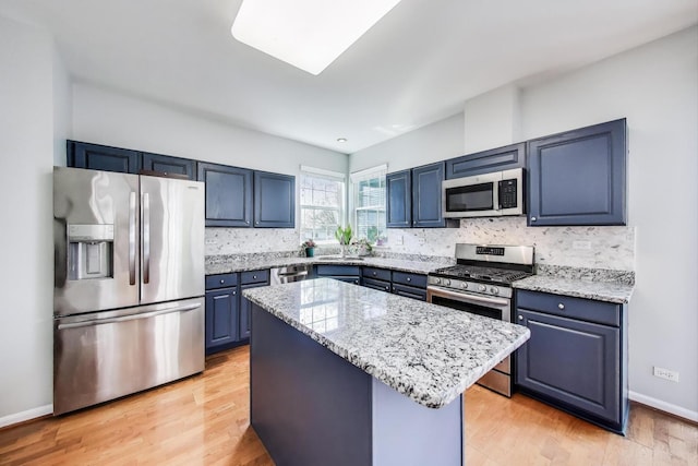 kitchen featuring appliances with stainless steel finishes, light stone counters, decorative backsplash, a kitchen island, and blue cabinets